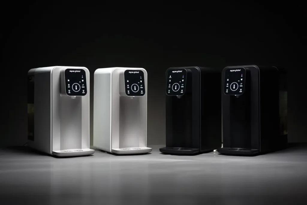 Vier elegante Wasserspender in Schwarz und Weiß, mit einem modernen Touchscreen-Bedienfeld, präsentiert auf einer dunklen, stilvollen Oberfläche.