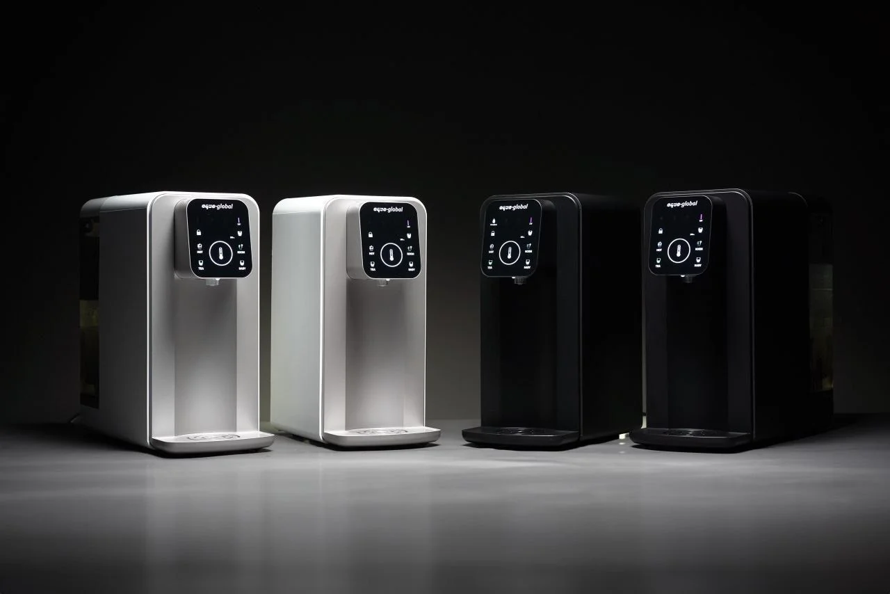 Vier elegante Wasserspender in Schwarz und Weiß, mit einem modernen Touchscreen-Bedienfeld, präsentiert auf einer dunklen, stilvollen Oberfläche.